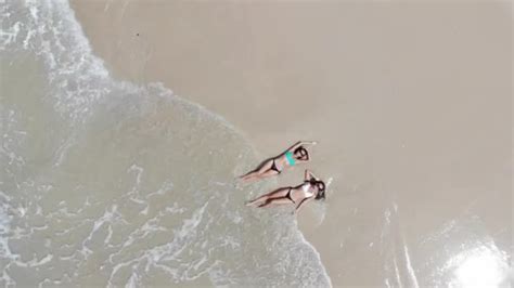 Top View Two Young Woman In A Bikini Lying And Relaxing On The White Sandy Beach With Turquoise