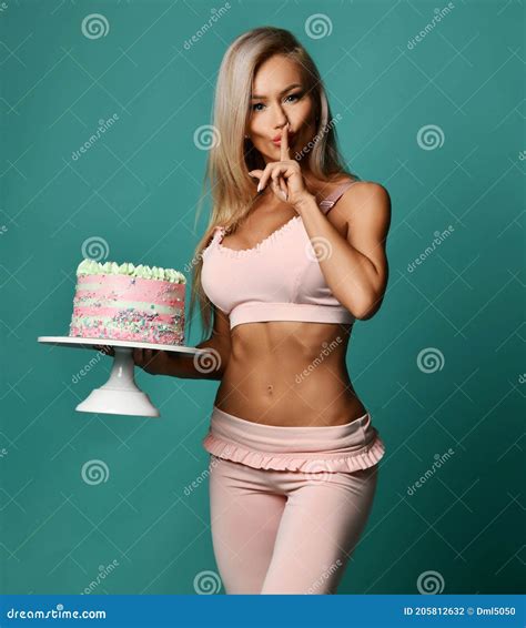 Slim Blonde Fitness Woman In Top Bra And Pants Stands Holding Big Cake In Hand And Gesturing