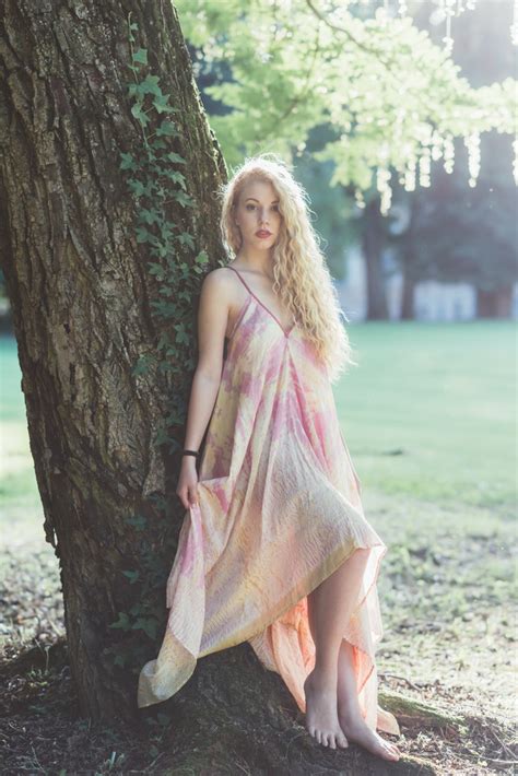 young beautiful blonde hair woman wearing pink dress standing   forest leaning   tree