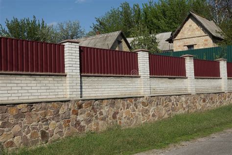 High Wall Fence Made Of Brown Stones White Bricks And Red Metal Stock