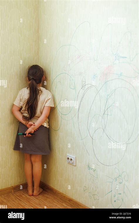 Portrait Of Little Naughty Girl Holding Marker Behind Back Standing Punished In Corner For