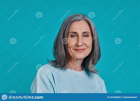 headshot of mature beautiful woman looking at camera and smiling while standing against blue