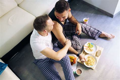 Gay Couple Eating Together Sitting On Their Living Room Floor Stock Photo Image Of Homosexual