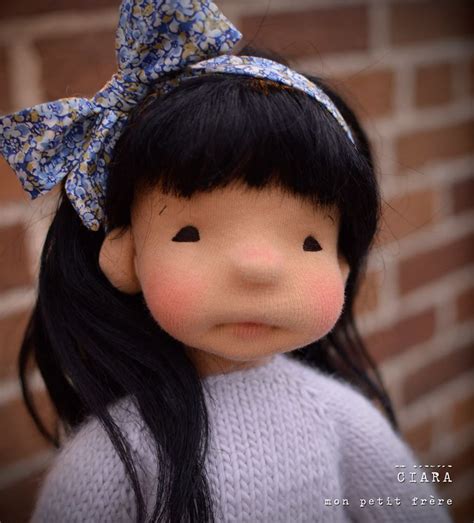 A Doll With Long Black Hair And A Bow On Her Head Is Standing In Front