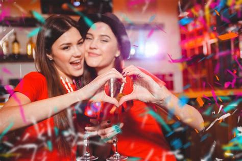 twee jonge lesbische meisjes kussen en maken een hart met hun handen bij een clubpartij stock