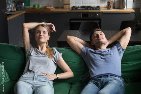 Young Man And Woman Sitting Together On Couch Sofa In Living Room Relaxing Leaning Back Wife
