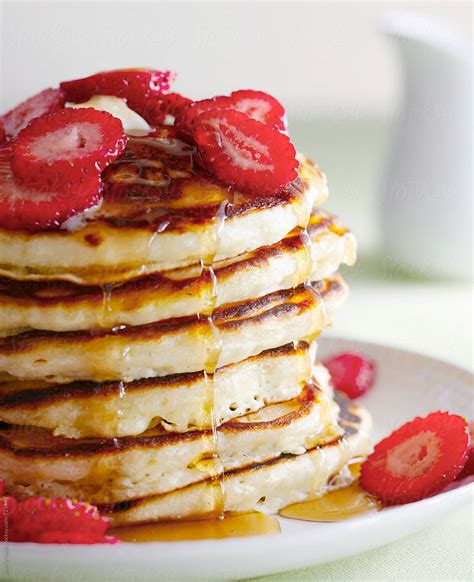 Stack Of Pancakes Topped With Strawberries And Dripping Syrup By