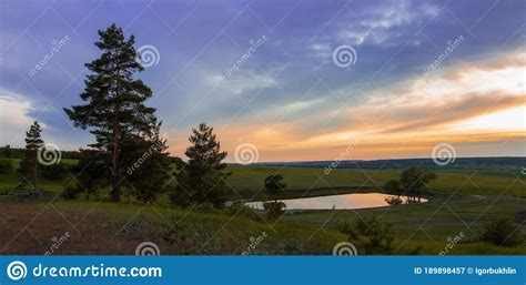 Lake At Sunset In The Forest Among Of Green Meadow And Dramatic Clouds