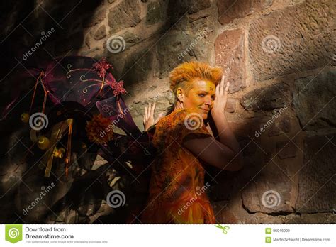 Woman In Orange Fairy Costume Leaning Against Castle Wall Stock Photo