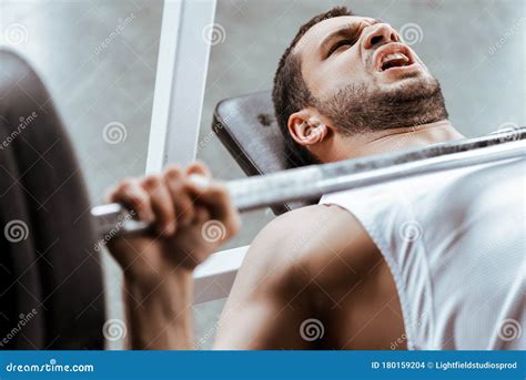 Focus Of Emotional Sportsman Working Out With Barbell In Gym Stock