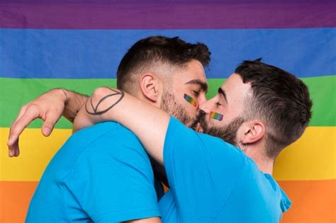 Pareja de hombres homosexuales abrazándose y besándose en la bandera del arco iris Foto Gratis