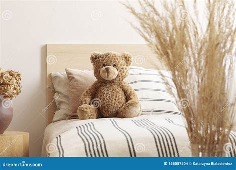 Brown Cute Teddy Bear On Single Wooden Bed With Striped Bedding Stock