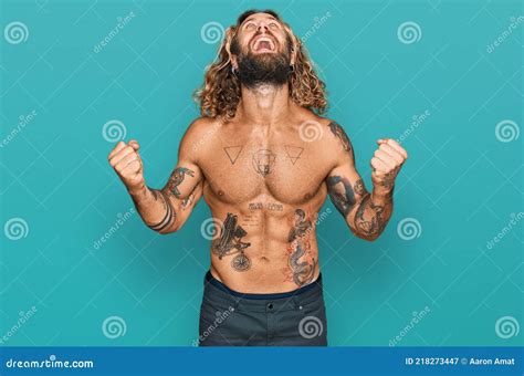 handsome man with beard and long hair standing shirtless showing tattoos crazy and mad shouting