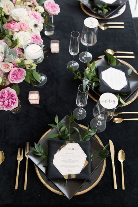 The Table Is Set With Black Linens Gold Chargers And Pink Flowers In Vases