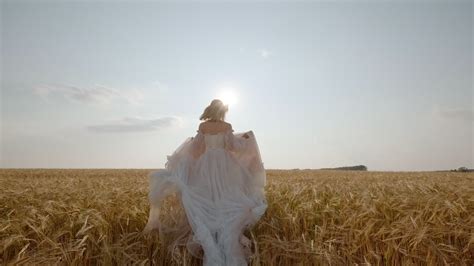 Young Woman Running Through A Wheat Field In A Fluttering Dress Back