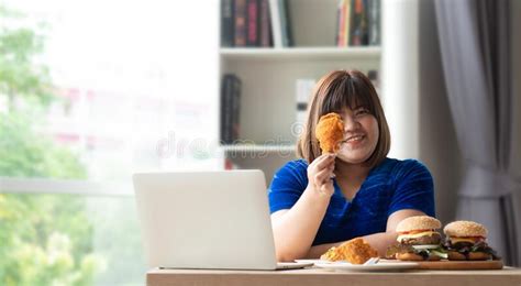 hungry overweight woman holding fried chicken hamburger on a wooden plate and pizza on table