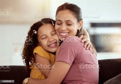 혼합 인종 미혼모와 딸이 가정 거실에서 포옹합니다 웃는 히스패닉 소녀가 라운지에서 한 부모를 포용하고 유대감을 느낍니다 주말에
