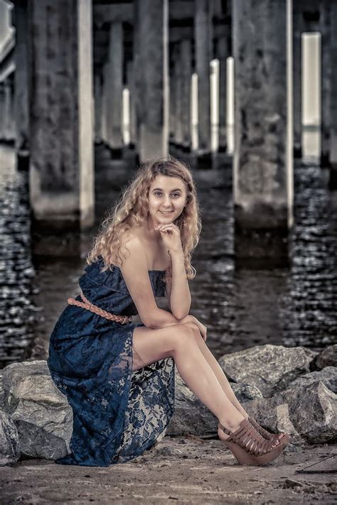 A Woman In A Blue Dress Is Sitting On Rocks Near The Water And Looking