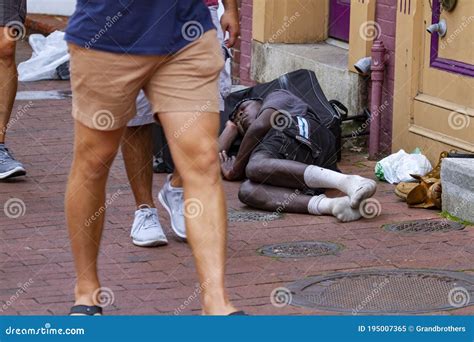 An Old African Homeless Man Is Sitting On A Bench By A Red Brick Wall