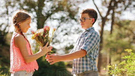Boy Giving Flowers To A Girl Standing In A Park Side View Of Kids In