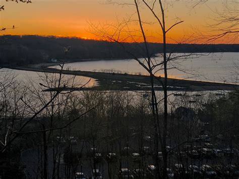 the sun is setting over a body of water with many trees in front of it
