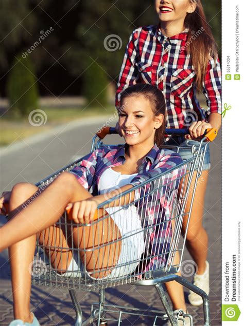 Two Happy Beautiful Teen Girls Driving Shopping Cart Outdoors Stock