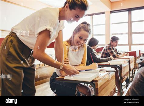 Happy Female Teacher Assisting Teenage Student In The Classroom Female