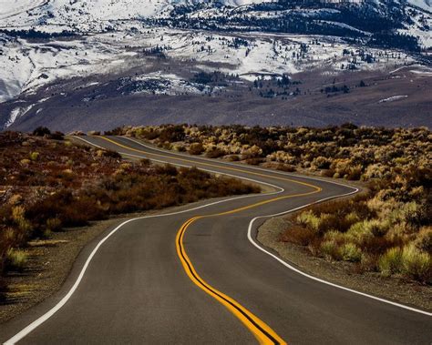 Long Empty Winding Road With Snowy Mountains In The Background