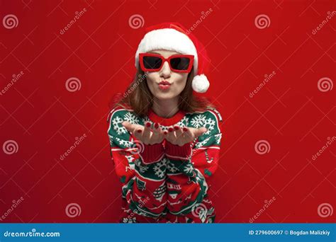Cute Girl In Christmas Sweater And Santa Hat In Glasses Sends Air Kiss