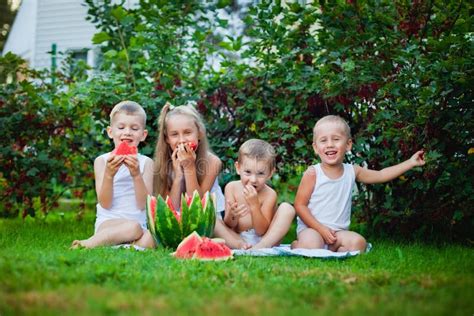 Four Children In White In Nature Sit On The Grass Funny Children Eat