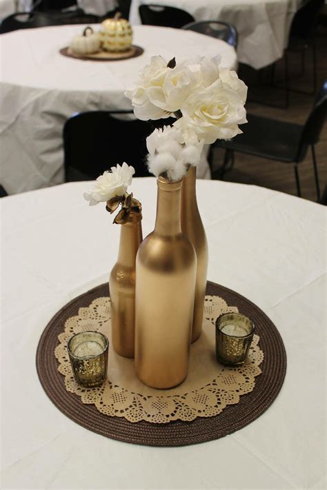 Three Gold Vases With White Flowers In Them On A Doily At A Table