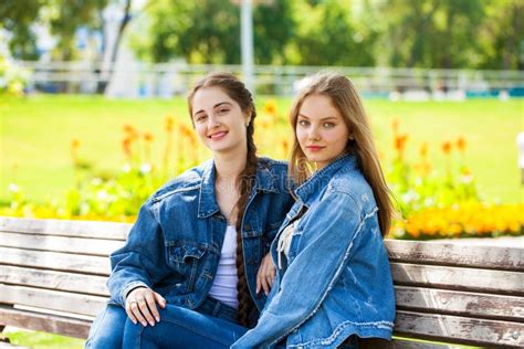 Two Beautiful Girlfriends Are Talking In A Park Sitting On A Bench