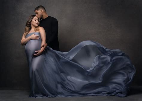 A Pregnant Woman In A Blue Gown Poses With Her Husband