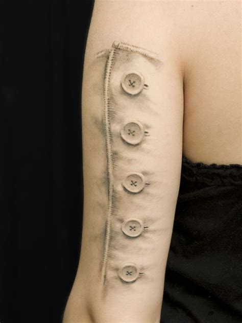A Woman With A Tattoo On Her Arm That Has Buttons In The Middle Of It