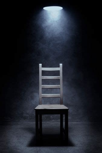 A Wooden Chair Sitting In The Dark Under A Light