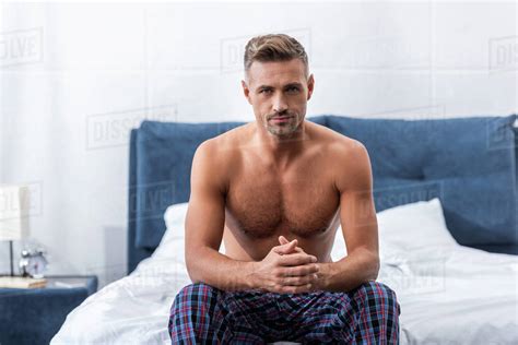 Confident Shirtless Adult Man Looking At Camera And Sitting On Bed At Home Stock Photo Dissolve
