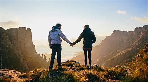 Young Hiking Couple Holding Hands Enjoying The Sunrise Over An Epic