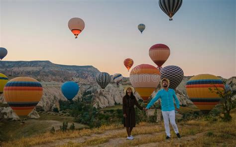 Happy Young Couple During Sunrise Watching The Hot Air Balloons Of
