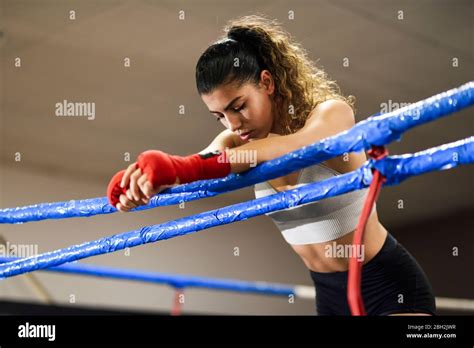 Athletic Female Boxer In Boxing Ring Leaning On Rope Concentrating