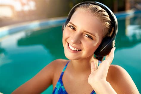 relaxed smiling woman listening to music in headphones bathing in swimming pool blonde girl