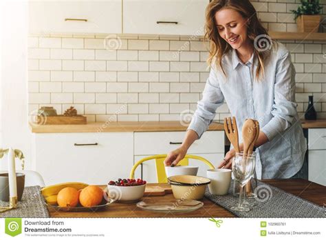 Young Smiling Housewife Standing In Kitchen Near Table Is Cooking