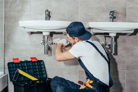 Back View Of Young Professional Plumber Fixing Sink In Bathroom Stock
