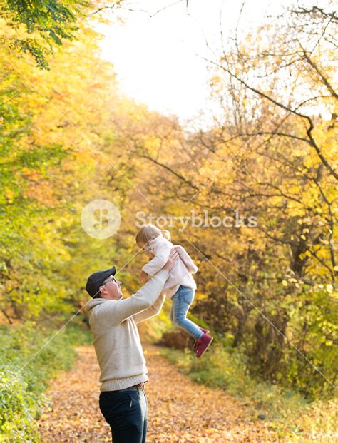 father holding his little daughter throwing her in the air walk in colorful autumn forest