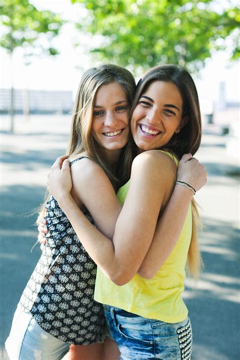Young Female Friends Embracing Together Standing In A Park By