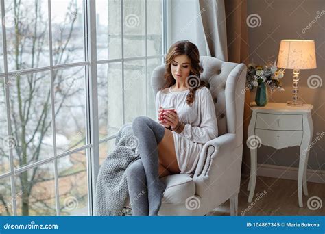 A Beautiful Slender And Brunette Girl Sits Near A Large Win Stock Image