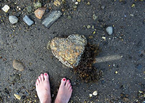 Womans Feet Stand Next To A Heart Shaped Rock Covered In Barnacles And