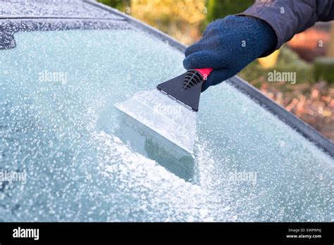 Hand Wearing Glove Scratching Ice From Car Window With Frost In Winter