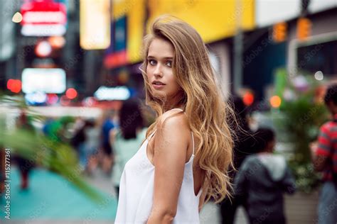 beautiful blonde sexy tourist girl walking in busy city street with long hair flying on the wind