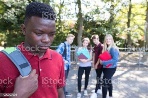 Unhappy Teenage Boy Being Gossiped About By School Friends Stock Photo