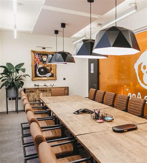 A Conference Room With Large Wooden Table And Black Lamps Hanging From